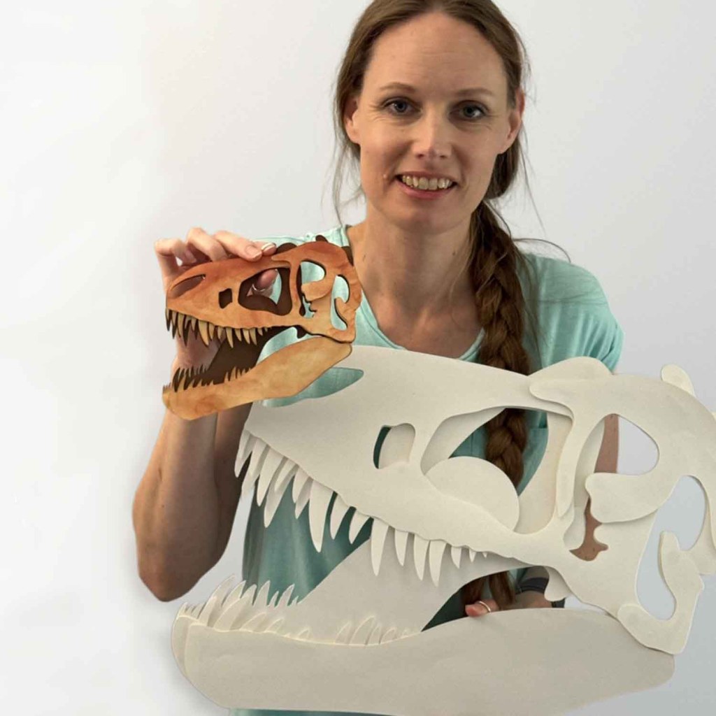 Cassandra is holding a small and large cardstock cut out of a TRex skull.