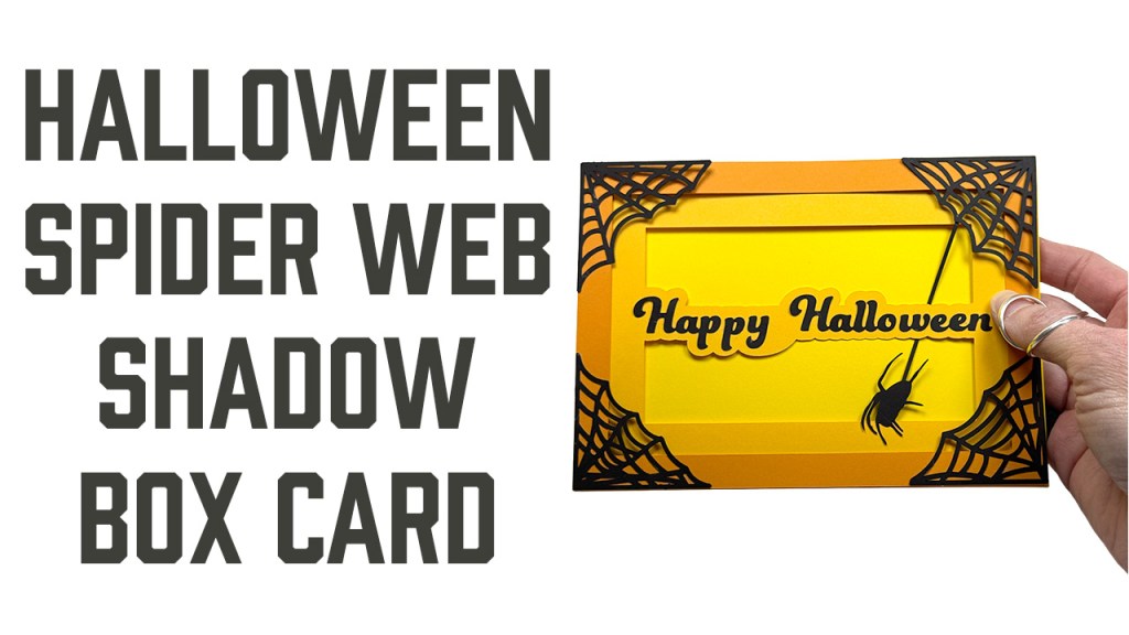A 5x7 greeting card in dark medium and light orange layers that reads "happy Halloween". each corner has a black spider web with a spider dangling from the top right web